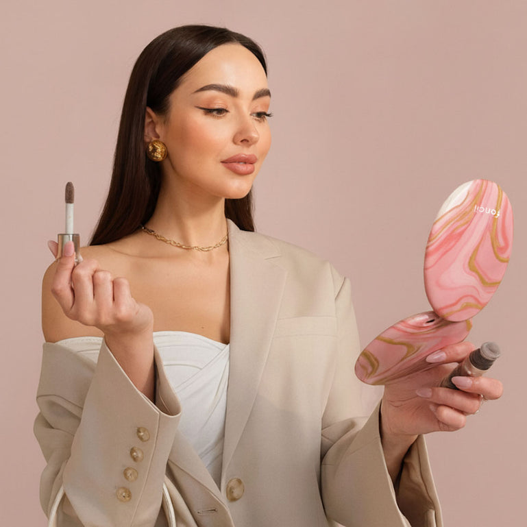 Taylor Lighted Compact Mirror with 10x Magnifying by Fancii & Co. open and lit up held by model in MARBLE ROSÈ