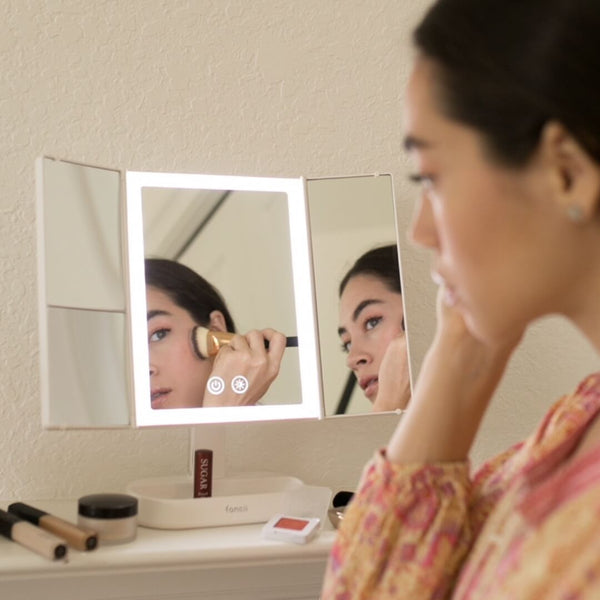 Woman using the Zora tri fold vanity mirror with LED lights by Fancii and Co with multiplle magnification options