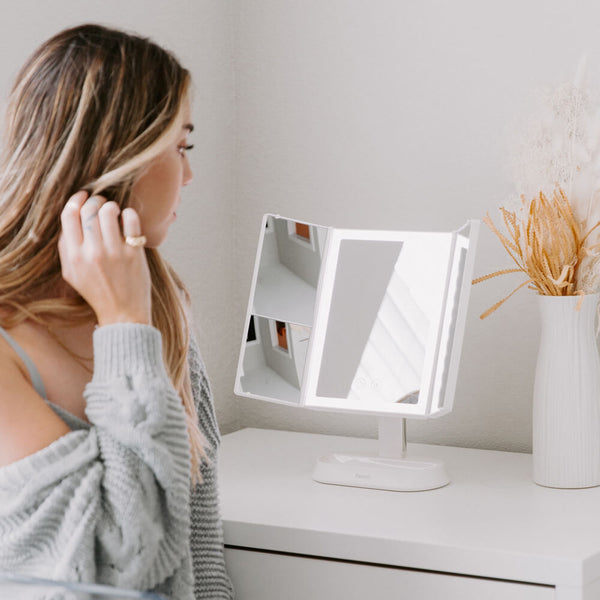 Woman using the Zora tri fold vanity mirror with LED lights by Fancii and Co with multiplle magnification options