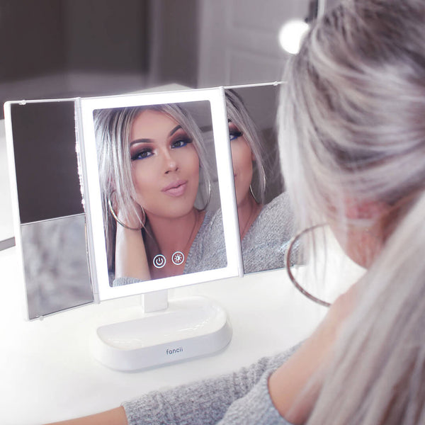 Woman using the Zora tri fold vanity mirror with LED lights by Fancii and Co with multiplle magnification options