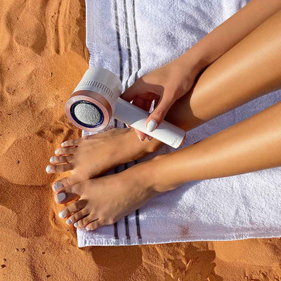 Female using Cali callus remover for feet in white at the beach by Fancii and co