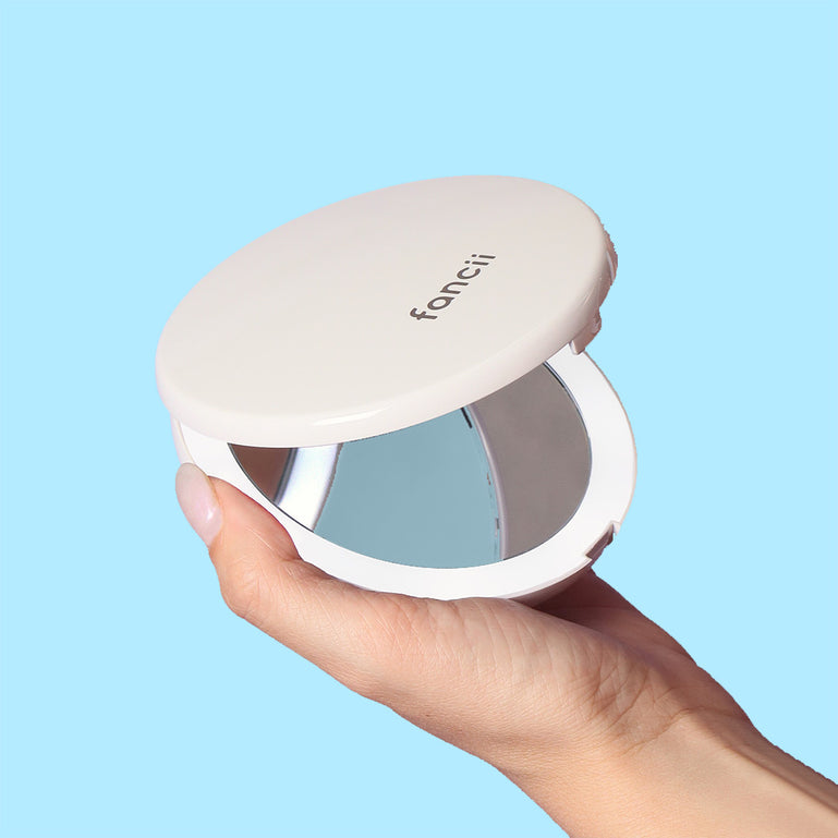 Woman holding a Mini Lumi LED compact mirror with 1x/10x magnifying by Fancii and Co_Silk White