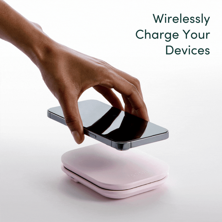 Mica Lighted Compact with built-in powerbank in Strawberry Cream color by Fancii and Co. A hand is placing a cell phone on the Mica showing how the mirror can charge your devices.