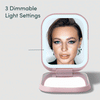 Mica Lighted Compact with built-in powerbank in Strawberry Cream color by Fancii and Co. Mirror is showcasing the 3 dimmable light settings with a female model looking in the mirror.