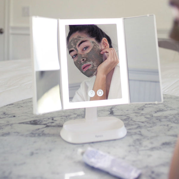 Woman using the Woman using the Zora tri fold vanity mirror with LED lights by Fancii and Co to apply skincare