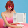 Woman using the Zora tri fold vanity mirror with LED lights by Fancii and Co